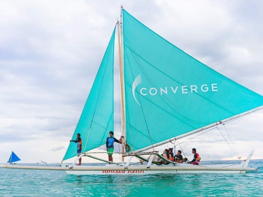 A boat with a teal sail on which the Converge logo is printed