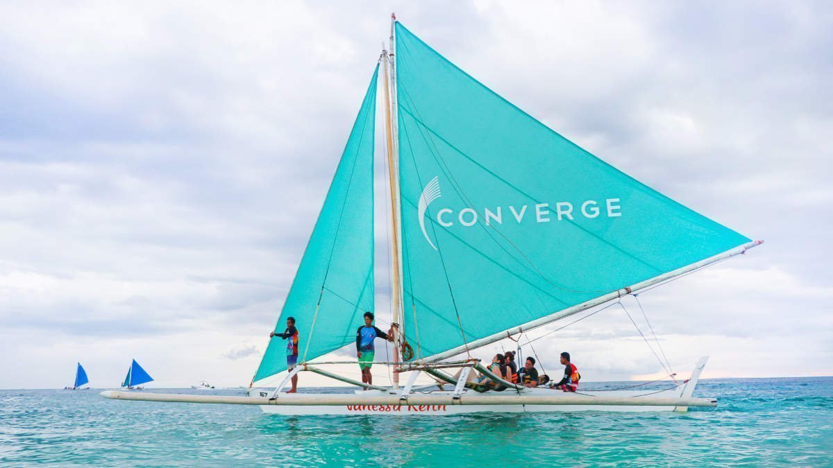 A boat with a teal sail on which the Converge logo is printed